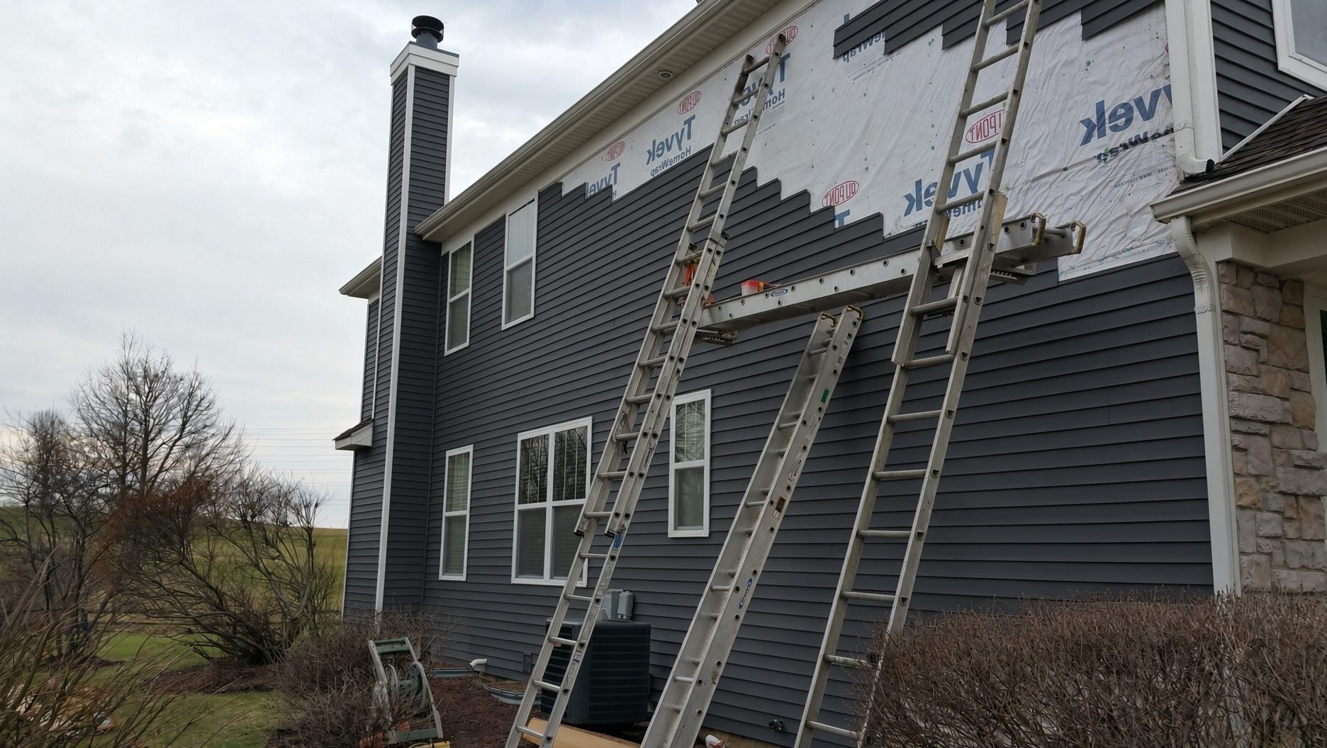 Ladders against a house with new gray siding and house wrap